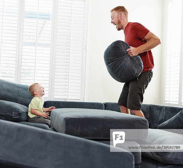 Vater mit Kissen spielt mit Sohn im Wohnzimmer