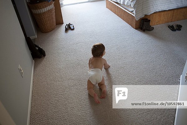 High angle rear view of baby boy wearing nappy crawling on carpet in bedroom