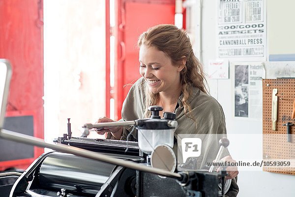 Female letterpress printer preparing printing machine in workshop