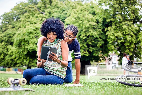 Junge und Mutter lesen gemeinsam digitales Tablett im Park