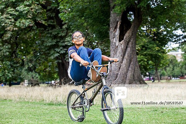 Boy riding BMX bicycle with feet up in park