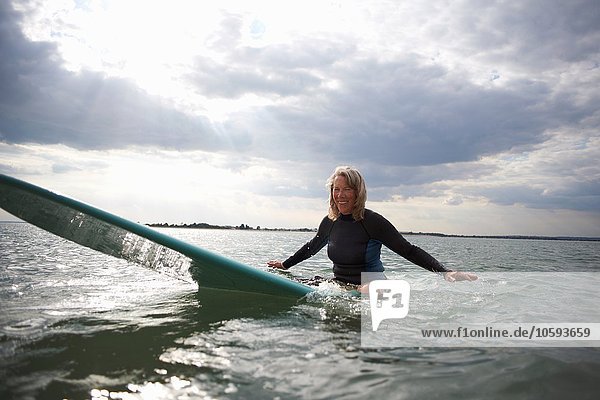 Porträt einer älteren Frau  die auf dem Surfbrett im Meer sitzt  lächelnd
