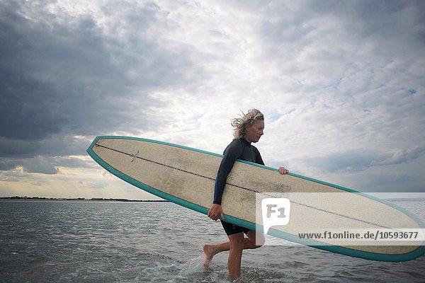 Ältere Frau  die vom Meer geht und Surboard trägt.