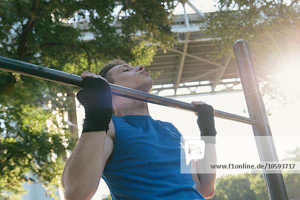 Junger Mann der trainiert und Klimmzüge an der Stange macht.