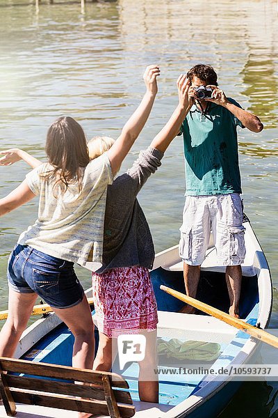 Young man in boat on lake photographing women