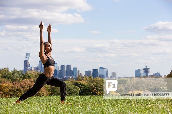 Side view of young woman on grass in yoga position  arms raised  eyes closed  Philadelphia  Pennsylvania  USA