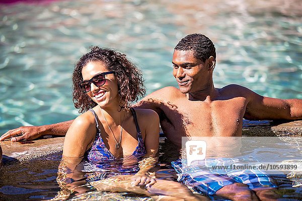 Couple sitting in swimming pool looking away smiling