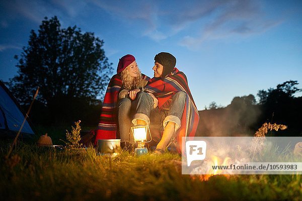 Junges Camping-Pärchen am Lagerfeuer in der Abenddämmerung
