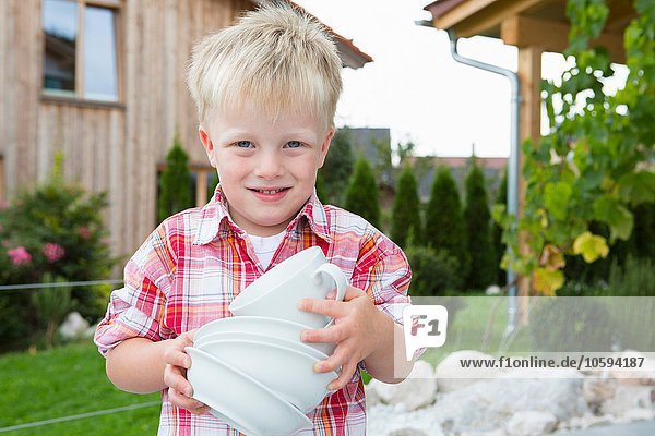 Portrait of boy in garden carrying stack of bowls