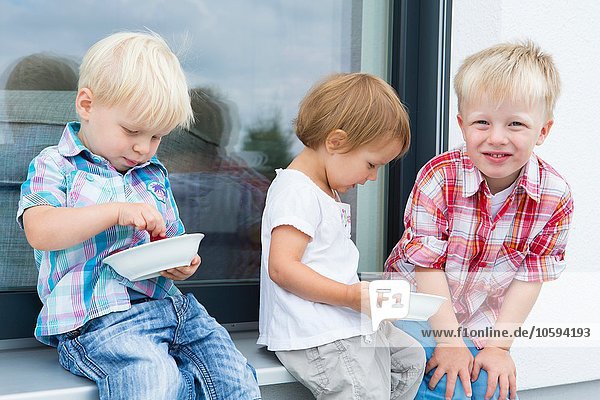 Weibliches Kleinkind und zwei junge Brüder auf der Terrasse,  die Schalen mit Himbeeren essen.