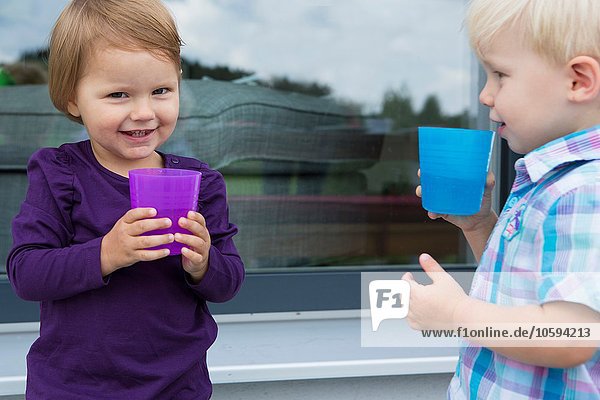 Boy and female toddler drinking from plastic cups on patio