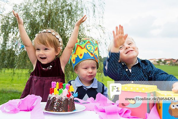Female toddler and two young brothers at birthday party in garden