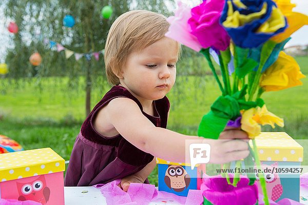 Female toddler with paper flowers at birthday party in garden