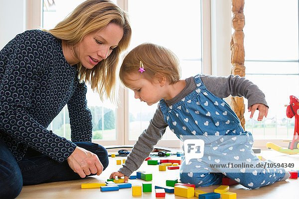 Female toddler and mother playing with building bricks on living room floor