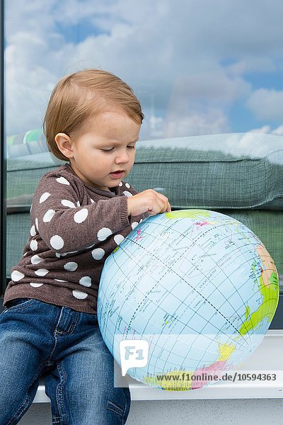 Female toddler playing with inflatable globe on windowsill