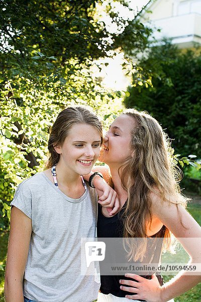 Zwei Teenager-Mädchen flüstern im Garten