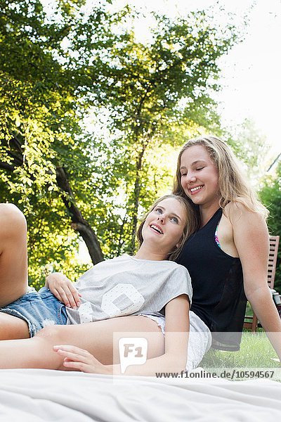 Zwei Teenagermädchen auf Picknickdecke im Garten liegend