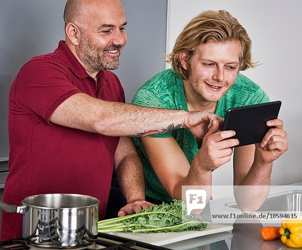 Männliches Paar mit digitaler Tablette bei der Zubereitung von Speisen in der Küche