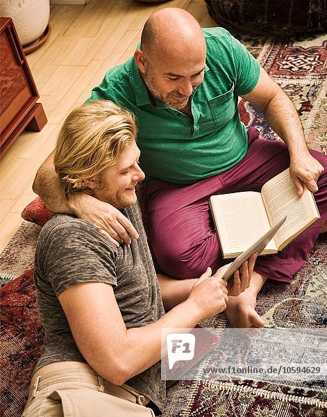 Männliches Paar sitzt auf dem Wohnzimmerboden und schaut auf ein digitales Tablett.