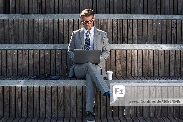 Geeigneter junger Geschäftsmann beim Tippen auf dem Laptop auf der Stadttreppe