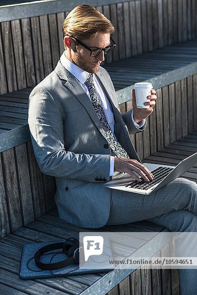 Junger Geschäftsmann beim Tippen auf dem Laptop auf der Stadttreppe