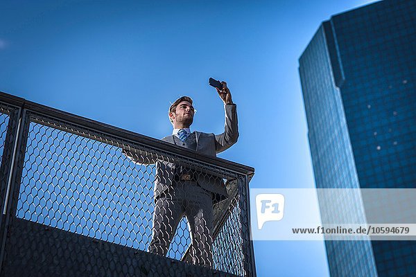 Flachwinkelansicht eines jungen Geschäftsmannes auf dem Smartphone auf dem Stadtbalkon New York USA