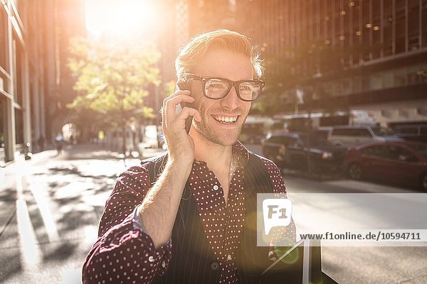 Fröhlicher junger Geschäftsmann beim Spazierengehen auf dem Smartphone  New York  USA