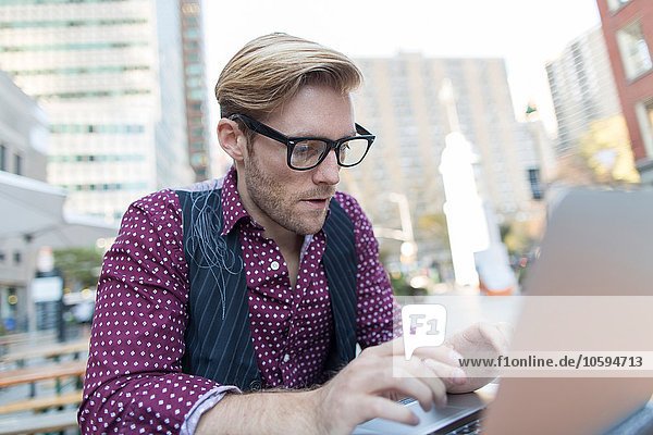 Gestresster junger Geschäftsmann beim Tippen am Laptop im Bürgersteigcafé  New York  USA