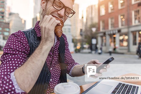 Gestresster junger Geschäftsmann beim Essen im Straßencafé New York USA