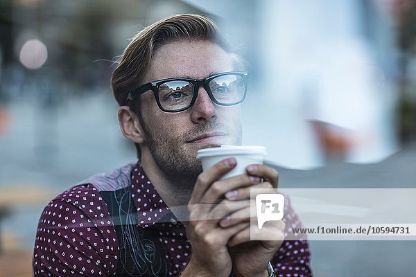 Trauriger junger Geschäftsmann hinter dem Stadtfenster der Kaffee zum Mitnehmen trinkt.