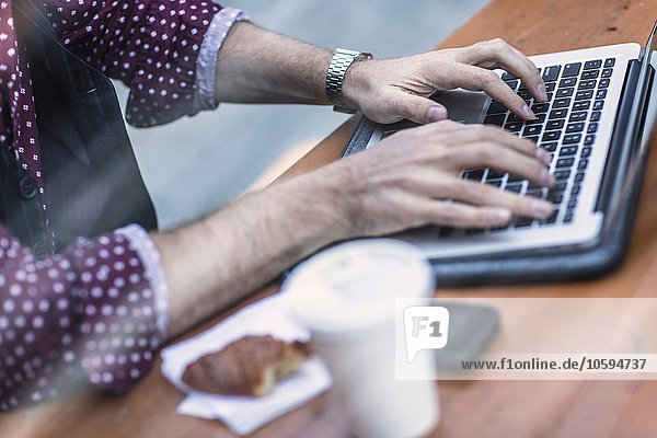 Beschnittene Ansicht des jungen Geschäftsmannes der auf der Laptop-Tastatur im Bürgersteigcafé tippt.