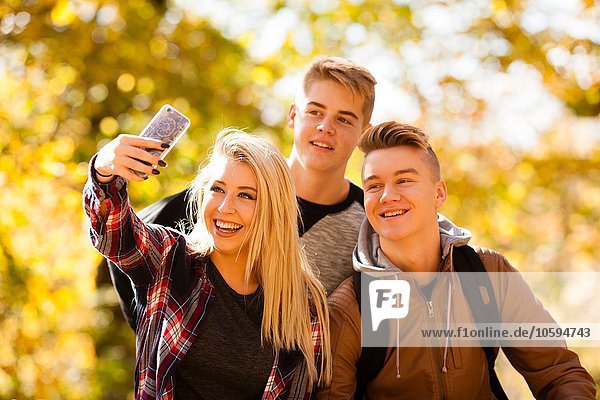 Junge Frau nimmt Selfie mit zwei Teenager-Brüdern im Herbstwald mit.