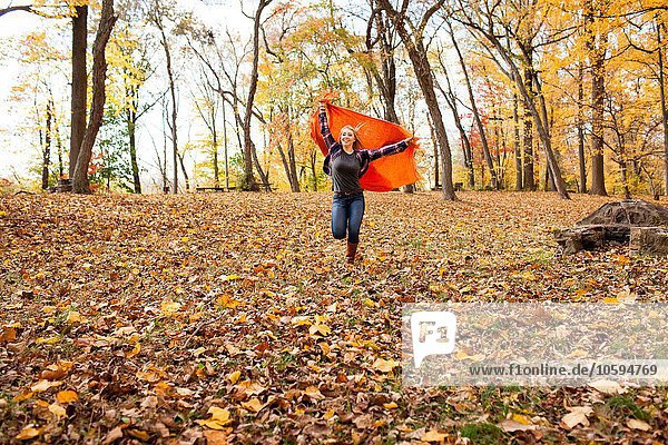 Junge Frau läuft und hält Decke im Herbstwald hoch