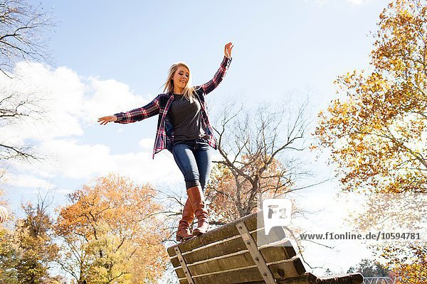 Young woman balancing on top of park bench in autumn forest