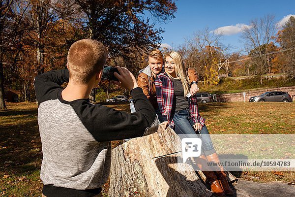 Teenage boy photographing brother and adult sister in autumn park