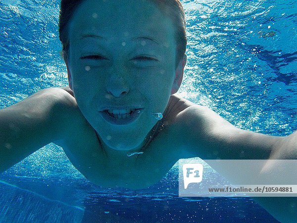 Nahaufnahme des Jungen  der im Schwimmbad unter Wasser schwimmt.