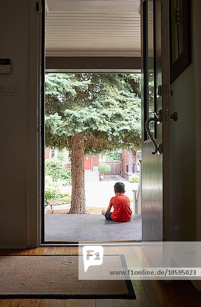 Junge sitzend auf der Vordertreppe des Hauses  Rückansicht