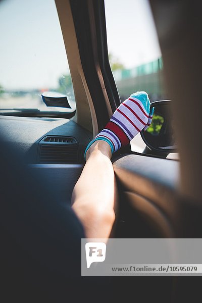 Bein mit bunt gestreiften Socken am Autofenster