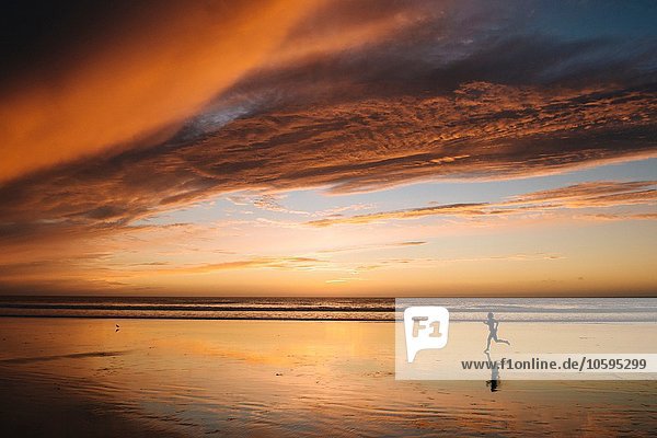 Seitenansicht der nackten Frauensilhouette am Strand unter dramatischem Himmel bei Sonnenuntergang