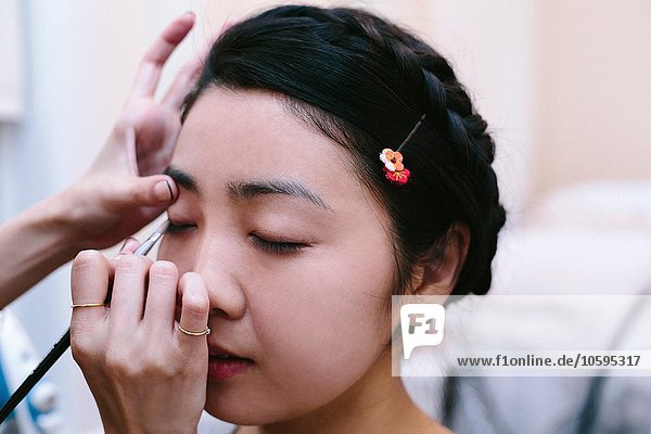 Hände des Maskenbildners beim Auftragen von Make-up auf eine junge Frau mit geschlossenen Augen