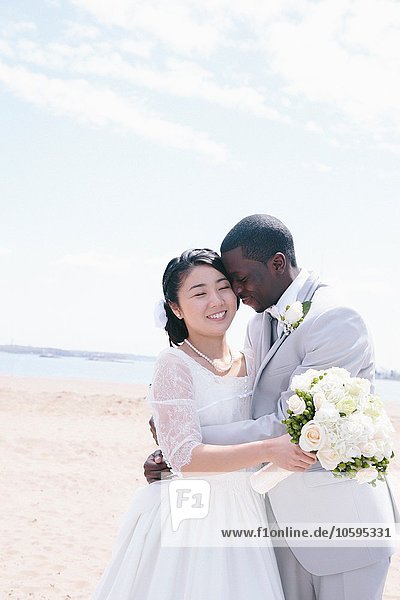 Bride and bridegroom on beach holding bridal bouquet hugging  smiling