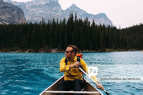 Front view of mid adult man paddling canoe  looking away  Moraine lake  Banff National Park  Alberta Canada