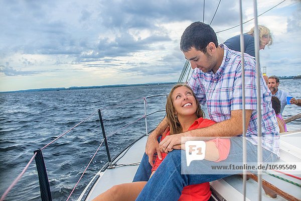 Young woman sitting between young mans legs on sailboat  face to face smiling
