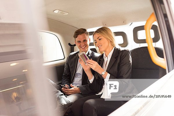 Businessman and businesswoman using smartphone in black cab  London  UK