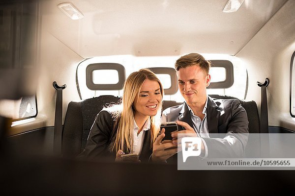 Geschäftsmann und Geschäftsfrau mit Smartphone im schwarzen Taxi  London  UK
