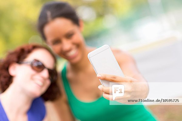 Junge Frauen nutzen Smartphone  um Sefie lächelnd in den Vordergrund zu stellen.