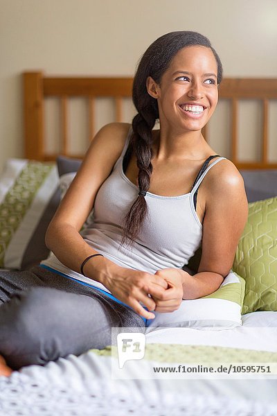 Young woman sitting on bed  hair plaited  looking away smiling