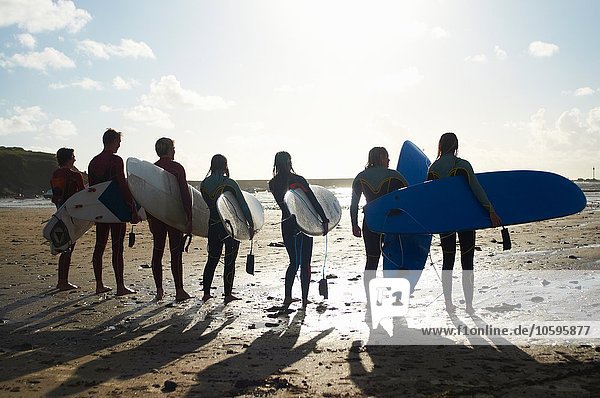 Surfergruppe  am Strand stehend  Surfbretter haltend  Rückansicht