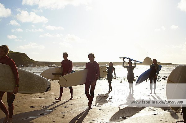 Gruppe von Surfern  am Strand spazieren gehen  Surfbretter tragen