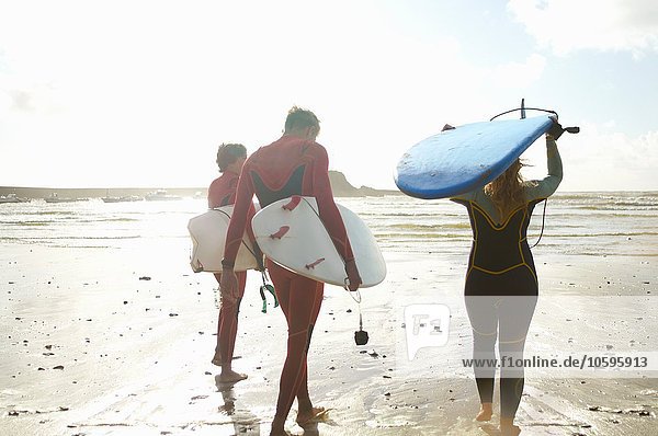 Group of surfers heading towards sea  carrying surfboards  rear view